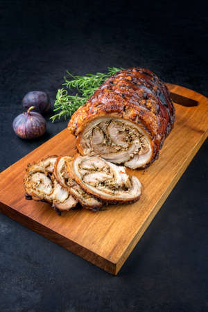 Traditional Italian Porchetta arrotolata pork meat sliced and as piece with herbs and figs offered as close-up on a modern design wooden boardの写真素材