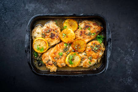 Traditional Italian deep-fried chicken piccata with capper and lemon slices offered as top view in a rustic old roasting pan with copy spaceの写真素材