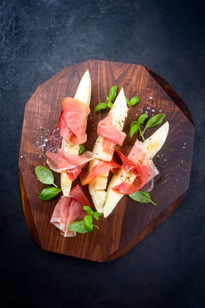 Traditional Italian antipasti with prosciutto di Parma and honeydew melon slices offered as top view on a wooden design board with copy spaceの写真素材