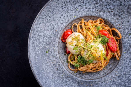 Modern design traditional fried scallops with tomatoes, broccoli pesto and Italian spaghetti pasta served as top view on a Nordic design plate with copy space leftの写真素材