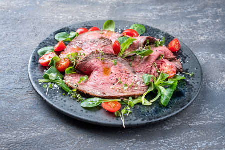 Modern style traditional Commonwealth Sunday roast with sliced cold cuts roast beef served with tomatoes and corn lettuce as close-up on a Nordic design plateの写真素材