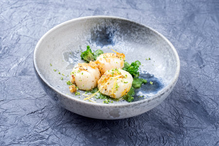 Modern style fried scallops with crumbles and lemon slices served with kalette cilanto relish as close-up on a Nordic design plate with copy spaceの写真素材