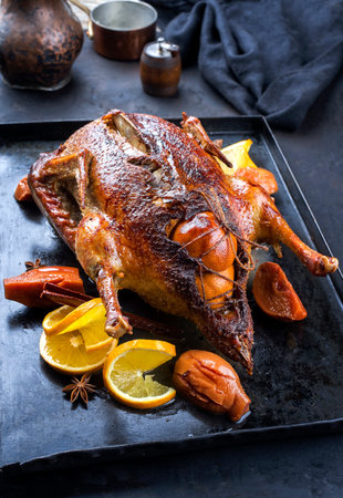 Traditional roasted stuffed Christmas duck with quinces and orange slices served as close-up on a rustic metal tray on a black boardの写真素材