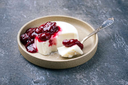 Modern style traditional blancmange almond pudding with sour cherry coulis served as close-up in a Nordic design plate on gray backgroundの写真素材