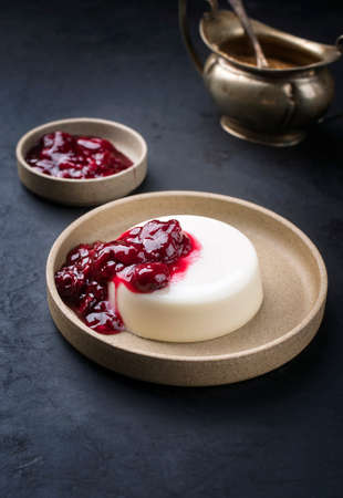 Modern style traditional blancmange almond pudding with sour cherry coulis served as close-up in a Nordic design plate on black backgroundの写真素材