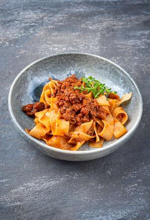 Modern style traditional Italian ragu alla bolognese sauce with papedelle pasta noodles and parmesan cheese served as close-up in a ceramic design bowl with copy spaceの写真素材