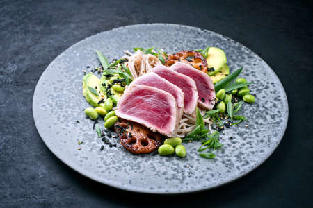 Modern style traditional Japanese gourmet seared tuna fish steak tataki with soba noodles and stir-fried vegetables served as close-up on a Nordic design plate with copy spaceの写真素材