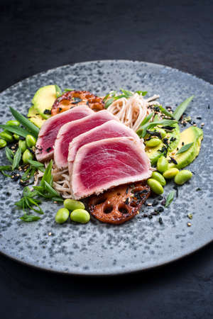 Modern style traditional Japanese gourmet seared tuna fish steak tataki with soba noodles and stir-fried vegetables served as close-up on a Nordic design plate with copy spaceの写真素材