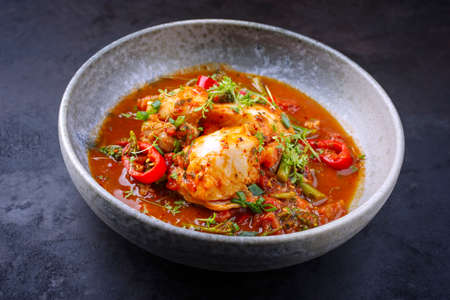 Modern style traditional Spanish seafood zarzuela de pescado with fish served in red sauce as close-up in a design bowlの写真素材