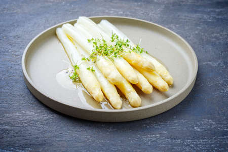 Modern style traditional steamed white asparagus with butter sauce hollandaise and cress served as close-up on a Nordic design plateの写真素材