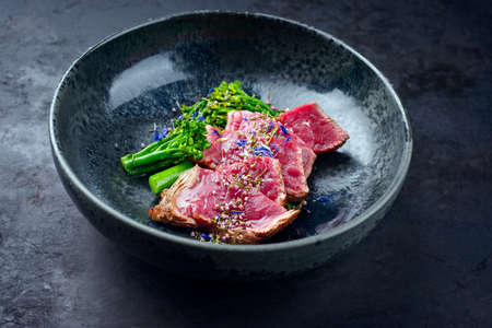 Modern style baby broccoli with fried dry aged sliced beef fillet steak served as close-up on a Nordic design plateの写真素材