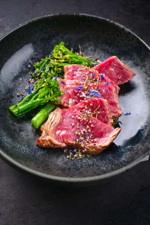 Modern style baby broccoli with fried dry aged sliced beef fillet steak served as close-up on a Nordic design plateの写真素材