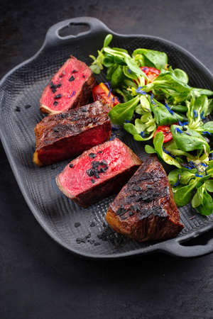 Rustic style barbecue dry aged wagyu roast beef steak with lambs lettuce and tomatoes served as close-up on a design skilletの写真素材