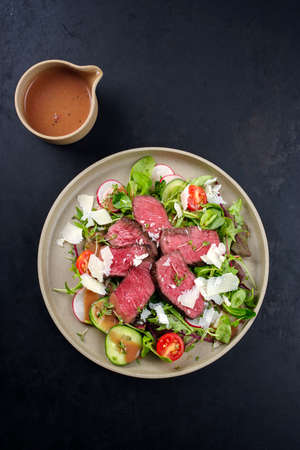 Modern style traditional fried dry aged bison beef rump steak slices with vegetable, lettuce and raspberry mustard dressing served as top view on a Nordic design plateの写真素材