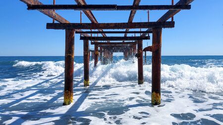 View of the breaking wave of a rusty metal pier. Seascape on a sunny day.の写真素材
