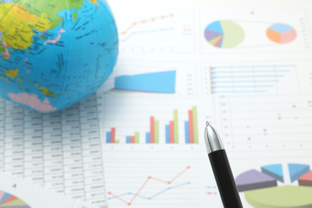 Pen in front of globe and papers with numbers and charts. Concept of workplace of the businessman. Pen in front of globe and papers with numbers and charts. Concept of workplace of the businessman.