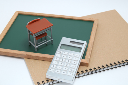 Miniature school desk, blackboard, calculator and notebook on white background. Education concept.の写真素材