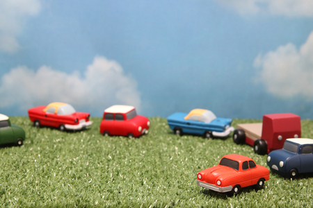 Miniature toy cars on green grass over blue sky and clouds. Traffic congestion.の写真素材