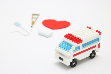 Toy ambulance car and abstract red heart on white background. Miniature drip, gibbs, and crutches.  Health, medicine, and cardiology concept. Health care, charity, donation concept.の写真素材