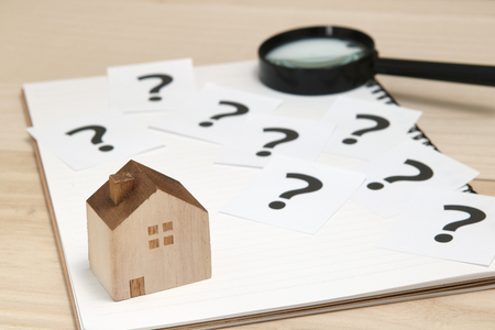 Miniature house and many question marks on white papers. House with question marks and magnifying glass. Real Estate Concept.の写真素材
