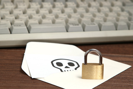 Lock in front of envelope with skull written on card resting computer keyboard. Data protection and cyber security concept.の写真素材