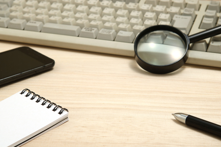 Business concept.  Memo pad, smart phone, and magnifying glass with computer keyboard. Workplace for the business person.の写真素材
