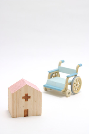 Miniature wooden hospital and wheelchair on white background. Concept of nursing care or assistance.の写真素材