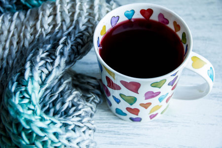 Love concept, cup of red tea, heart shape and knitted scarf on wooden floor.
