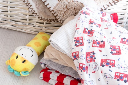 grey basket with children's toys, diapers, accessories on table on grey wooden background. Mother care. children's room, the pile of blue clothes for newborn boyの写真素材