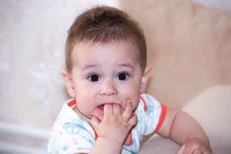 Baby boy plays with fingers in mouth and happy facial expression. Portrait of a crawling baby smiling. Teething infant playing. Newborn child at home. child scratching his teeth.の写真素材