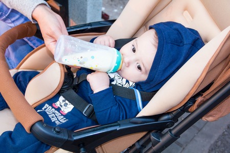 happy little baby sitting in a stroller and drinking from bottle milk, in winter clothes, the concept food breast .の写真素材