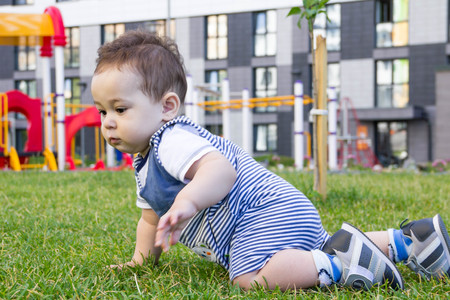 little baby learning to crawl on the grass a Sunny summer day. the concept children's development by months. happy child playing in the Playgroundの写真素材