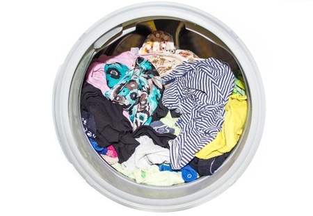 A close up of a modern washing machine loaded with clothes isolated on white background. Washing machine full of dirty clothes, closeup. ashing machine windowの写真素材