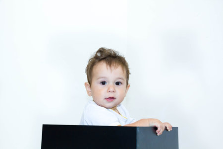 A young infant boy peeking out of box on a white background