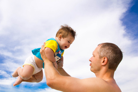 young happy father holding up in his arms little son putting him up at the beach in barefoot standing in front of sea waves wet sand having fun with kid in Summer sunset coast.の写真素材