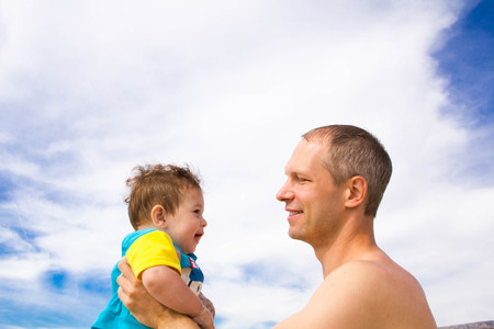 young happy father holding up in his arms little son putting him up at the beach in barefoot standing in front of sea waves wet sand having fun with kid in Summer sunset coast.の写真素材