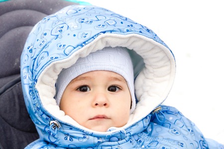 Happy laughing baby girl enjoying a walk in snowy winter park sitting in a warm stroller with sheepskin hoodの写真素材