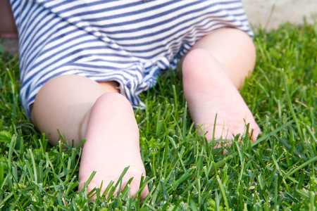 Cute baby crawling green grass. Rear view. Primary focus on baby feet.の写真素材