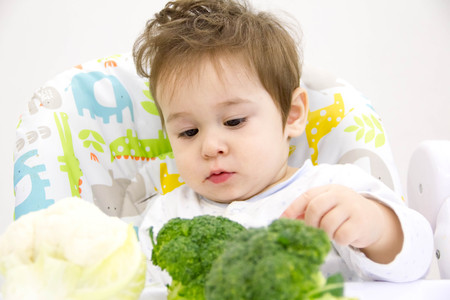 Cute baby eating broccoli sitting on floor indoorsの写真素材