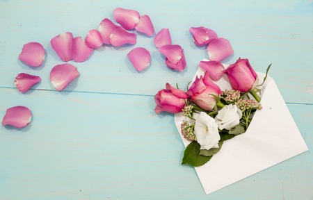 Beautiful roses and petals in the envelope on the worn wooden table, the concept love messages for women, greeting cardの写真素材