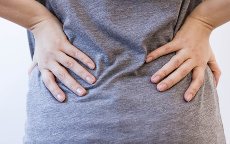 Attractive female person suffers from backache. All on white background. young woman with backache. injury woman stretches back pain backache, spinal . cause of Long working hours and health.の写真素材