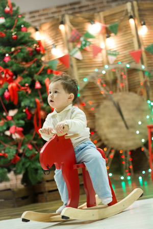Happy cute small boy riding wooden rocking horse in front of christmas tree and presentsの写真素材