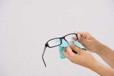 Glasses cleaning with fine microfiber cloth. Women hand cleaning glasses lens with blur green backgroundの写真素材