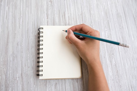 Woman's hands holding pencil and spiral notepad as mockup for your design. gray background, flat lay styleの写真素材