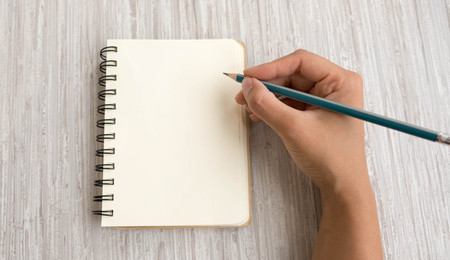 Woman's hands holding pencil and spiral notepad as mockup for your design. gray background, flat lay styleの写真素材