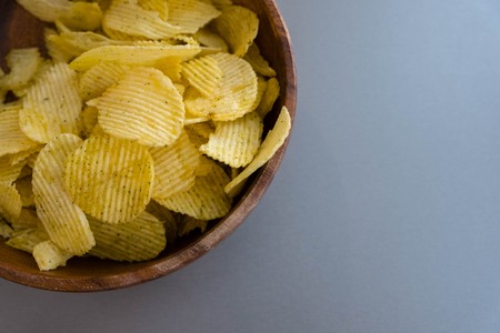 Potato chips in bowl on a grey background, top view. Salty crisps scattered on a tableの写真素材