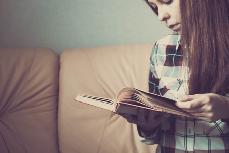 Young woman reading. Close up on woman hands turning page in vintage book. Woman read a book. Soft photo of female hands holding open book home interior background. Woman place her arms on her lapの写真素材