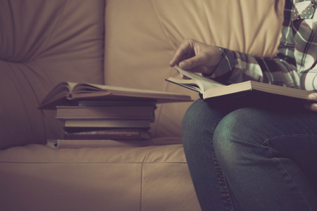 Young woman reading. Close up on woman hands turning page in vintage book. Woman read a book. Soft photo of female hands holding open book home interior background. Woman place her arms on her lapの写真素材