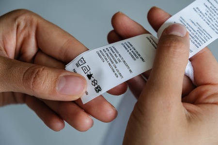 Woman checking the care label. selective focus. Woman's hands holding clothes label with cleaning instructions. lose-up Of Person Reading The Clothing Label Showing Washing Instructions.の写真素材