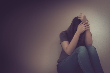 sadness young woman sitting on wood floor looking at empty dark area feeling unhappy and afraid on white wall background with battered abused woman concept.の写真素材